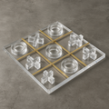 Angled view of lucite acrylic Tic Tac Toe board with gold grid and clear pieces on gray stone surface