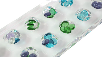 Close-up of green, blue, and purple glass beads in lucite Mancala board on white background