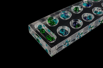 Lucite acrylic Mancala game board with green and blue beads on black background