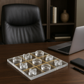 Lucite Tic Tac Toe board on a dark wood office desk next to laptop and notebook