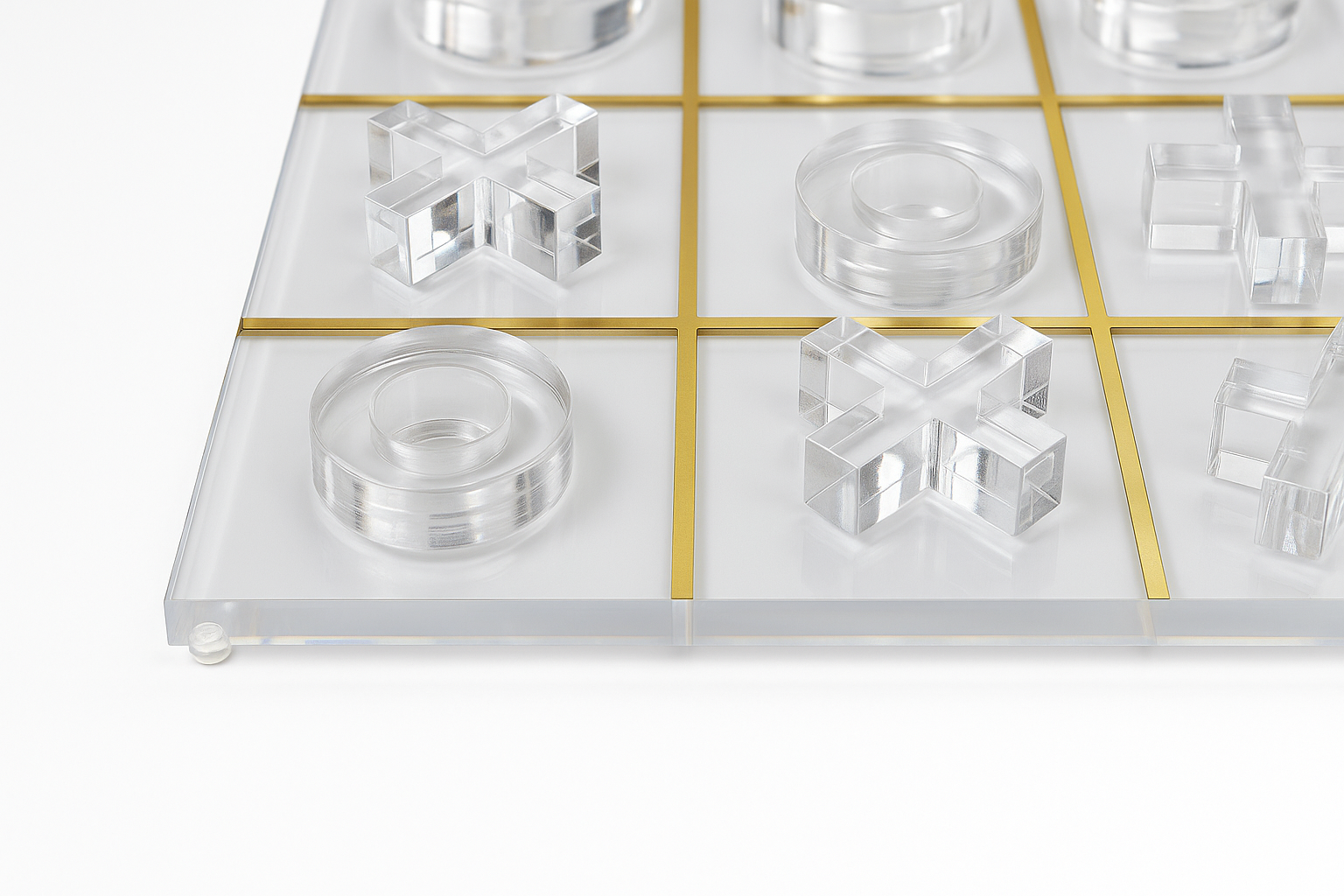 Close-up of lucite Tic Tac Toe game with gold grid and clear pieces on white background